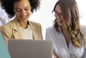 Two businesswomen reviewing content on a laptop and smiling