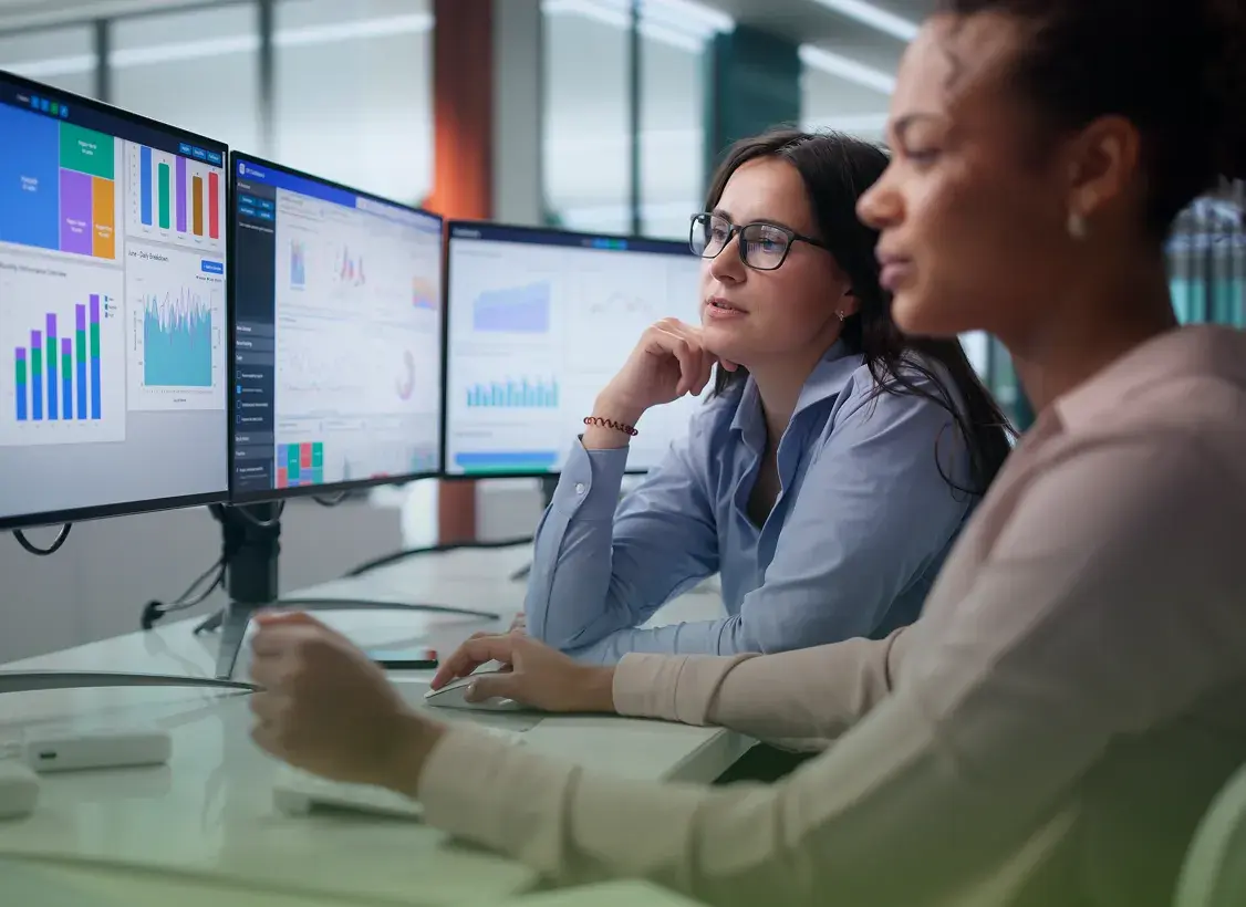Two analysts reviewing healthcare cost dashboards on multiple monitors